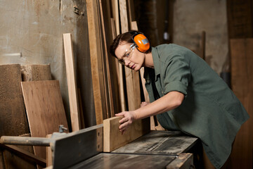 A dedicated carpenter skillfully shapes a wooden piece, surrounded by tools and raw materials in her workshop.