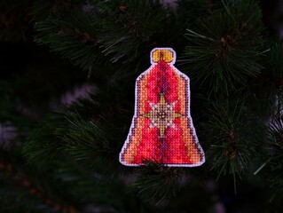 Red bell cross stitched Christmas ornament on Christmas tree.