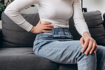 Abdomen inflammation, menstrual period. Flatulence ulcer young woman sitting on sofa holding on...