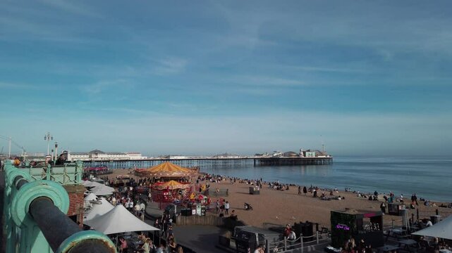 Busy day at a British seaside funfair and beach in Brighton. Visitors enjoy sunny weather, outdoor dining, and attractions in a relaxed atmosphere.