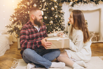 Happy couple exchanging christmas gifts near decorated tree