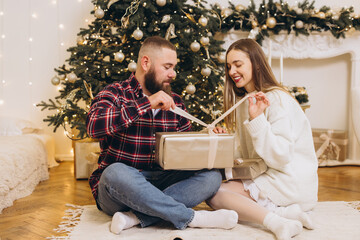 Couple opening christmas gift in front of decorated tree