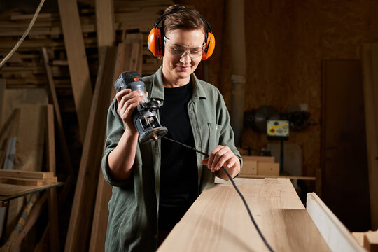 A skilled carpenter uses a router to craft wood with precision in her vibrant workshop.