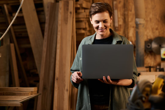 A skilled female carpenter explores design ideas on a laptop amid her woodworking workshop, showcasing her talent.
