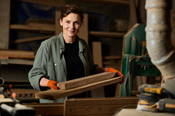 A talented woman expertly shapes wood while wearing gloves, showcasing her craftsmanship in a busy workshop.