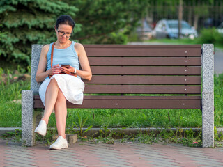 Caucasian woman is sitting casual wear on a bench at a park and looking to smartphone