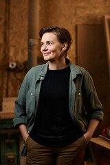 In a well-lit workshop, a female carpenter smiles confidently while surrounded by her woodworking tools and materials.