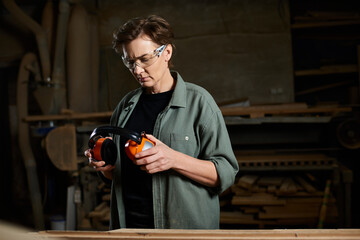 In her workshop, a dedicated female carpenter adjusts her protective gear while focusing on her craft.