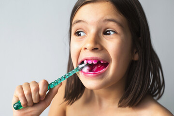 close-up portrait of 7 year old girl brushing teeth with toothbrush after applying pink solution to...