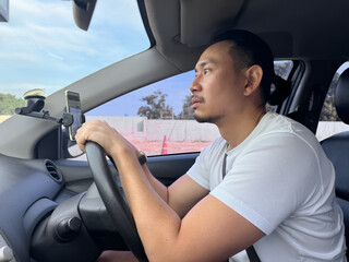 Side view of asian man with beard bun hair, top knot hairstyles, holding steering wheel while focus driving a car on road in city, rearview mirror, insurance concept.