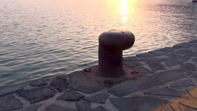 A bollard of the pier with the village in the background at sunset. Marina di Camerota, Salerno, Italy.