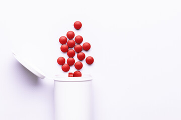 Big red medical tablets in white plastic container on white background close up. Tablets with cranberry extract for UTI treatment. Natural herbal therapy.