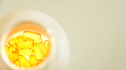 Golden Omega-3 fish oil softgel vitamins supplement pills inside a white bottle. Natural sunlight top view shot. Essential nutrients vitamins for a healthy life concept.