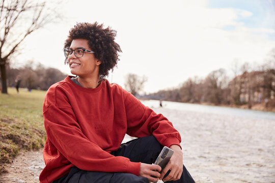Gen Z boy outside hanging around beside a river and smiling at the camera. Munich, Germany