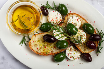 a plate with a snack, ciabatta bread with cheese and olives, olive oil, spices and herbs, top view, no people,