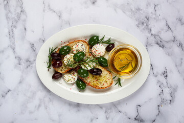 a plate with a snack, ciabatta bread with cheese and olives, olive oil, spices and herbs, top view, no people,