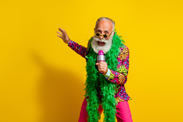 Portrait of nice elderly man hold microphone sing wear pink outfit isolated on yellow color background