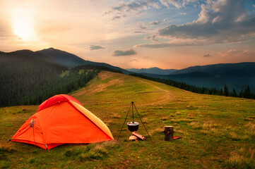 Orange tent on a meadow in the mountains at sunset. Cooking tent with a cauldron.
