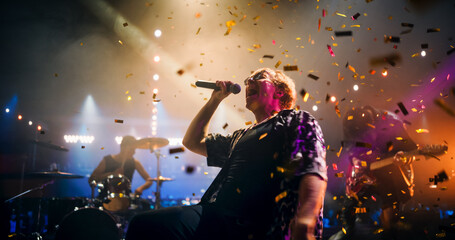 Professional Rock Musicians Performing Under Falling Confetti on Festival Stage, Playing Popular Rock Tracks in Front of a Crowded Concert Arena. Electrifying Performance at an Indoors Festival