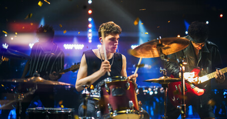 Handsome Young Drummer Performing on Concert Stage with His Band Members, Surrounded by Falling...