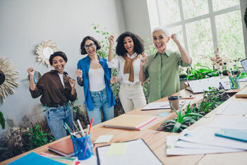 Photo of successful corporate women delighted raise fists modern interior office business center indoors