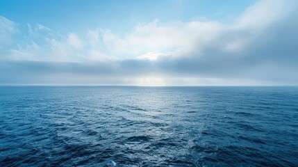 Obraz premium A vast expanse of blue ocean stretches to the horizon under a sky filled with fluffy white clouds.