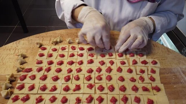 Chef wearing a white coat and gloves folds squares of dough over meat filling to make turkish manti ravioli