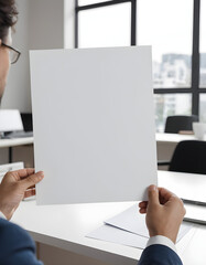 Person holding blank paper in bright modern workspace.