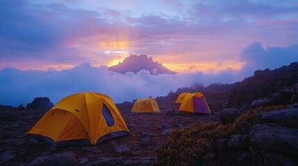 Three yellow tents pitched on a rocky mountainside with a mountain peak in the background at sunset.