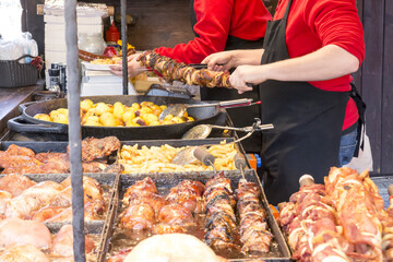 A man on the street fried on a large grill a lot of different meats and sausages during the street festival