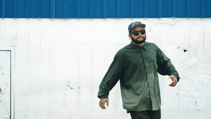 Hipster dancing b-boy foot step at street with blue wall. Asian break dancer practice street dance while stretch arms. Hip hop choreographer perform energetic dance. Outdoor sport 2024. Hiphop.