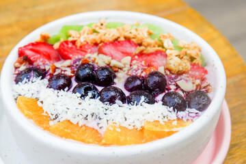 Acai bowl with strawberries, blueberries,orange,kiwi fruit,granola ,chia seeds and coconut flakes on wooden background,close-up, top view, space for text.