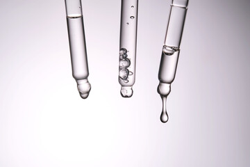 Three pipettes with a cosmetic product. Serum or fluid drips from one of them.