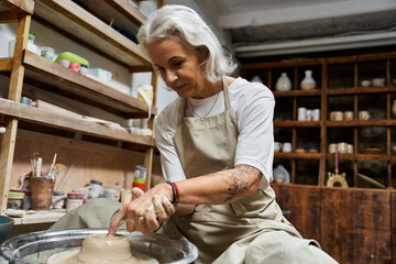 A mature woman skillfully molds clay on a pottery wheel, immersed in creative passion.