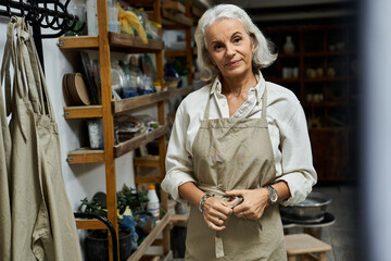 A mature woman with silver hair stands in her warm workshop, ready to create something beautiful.