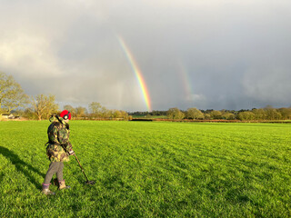 Woman searching with metal detector in grass field,  UK