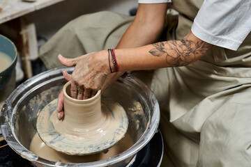 A skilled woman shapes clay on a potters wheel in her creative workspace.