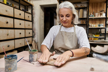 A talented mature woman shapes clay at her workspace, surrounded by creative tools.