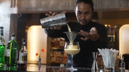 Asian bartender using strainer all ingredients alcohol liquor and syrup tasty in cocktail glass with ice serving special refresh drink showcasing nightlife mixology at luxurious nightclub. Vinosity.