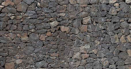 
Panoramic background of natural volcanic stone wall in dark gray and ochre tones, with irregular...