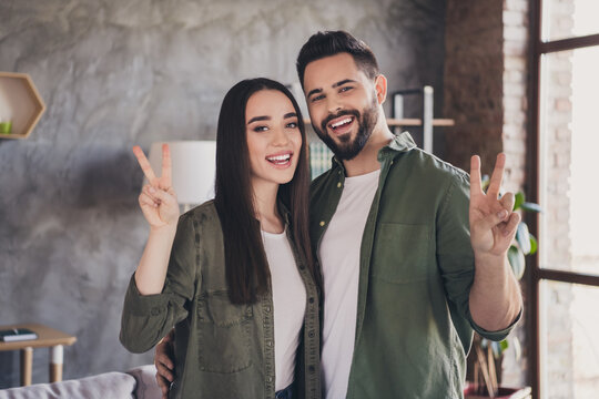 Photo of young attractive charming married people buy flat moving relocation cosy modern loft interior apartment indoors v-sign