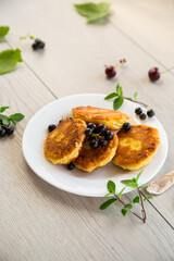 Fried curd cheese pancakes with black currants, on a wooden table