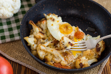 fried omelette with cauliflower and vegetables in a frying pan on a wooden table