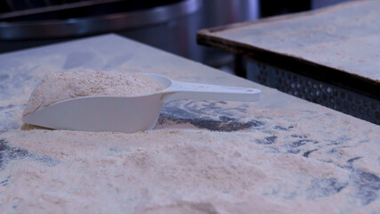 White scoop filled with flour on a baking workstation