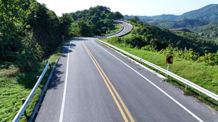 Aerial view highway Drone flying above winding road during sunlight, Winding asphalt road through tropical rainforest. countryside landscape. Landmark tourist attractions in Nan Province, Thailand.	