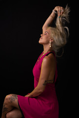 Beautiful Caucasian woman in red dress posing and touching her blonde hair. Isolated on black background. Salvador, Bahia.