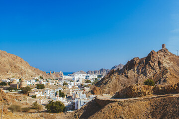 White houses between rugged mountains and cliffs. Muscat, Oman’s port capital, sits on the Gulf of Oman surrounded by mountains and desert.
