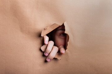 Man eye looking through a hole in a sheet of paper.