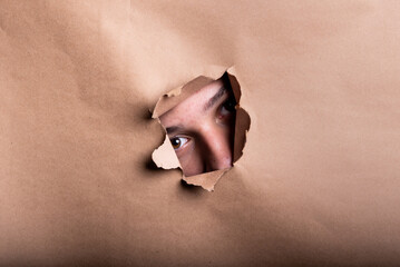 Man eye looking through a hole in a sheet of paper.