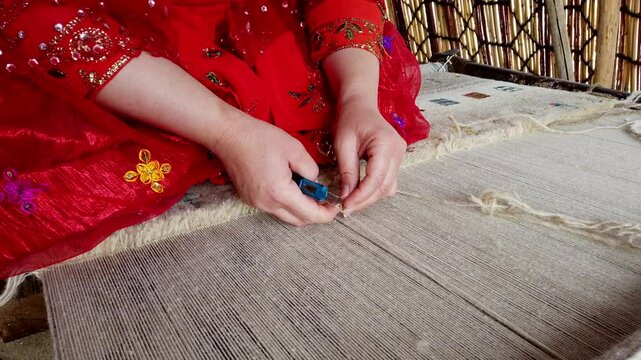 Craftswoman in a red dress ties knots on a traditional loom, showcasing the intricate art of carpet weaving